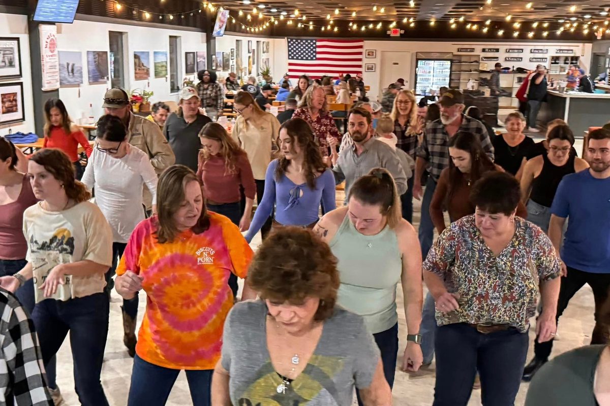 A packed line dance in the taproom under string lights and a US flag