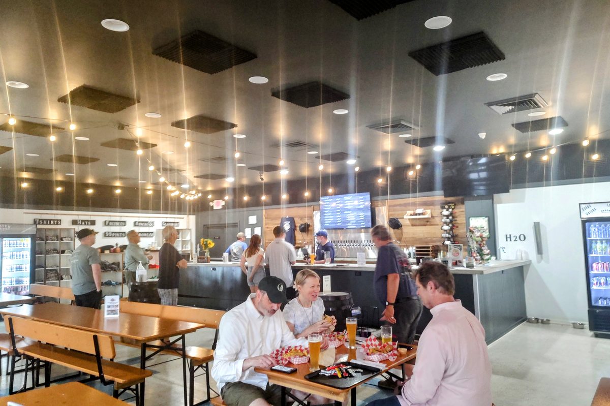 The taproom bar with a TV tap list and a merch wall, guests eating burgers in front